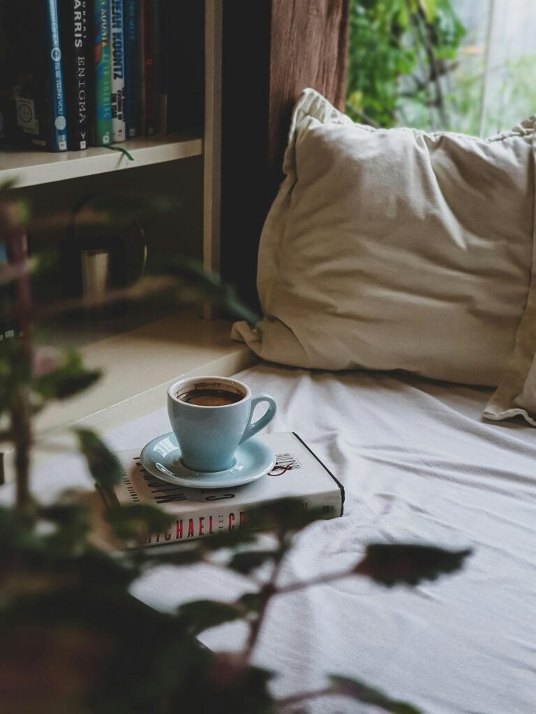 pexels-photo-8979738-8979738 A comforting scene featuring a warm cup of coffee resting on a book, set on a cozy bed by a bookshelf.